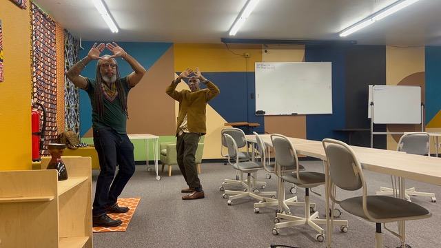 Heru TchaasAmen and a community member in a symbolic hand gesture, community classroom