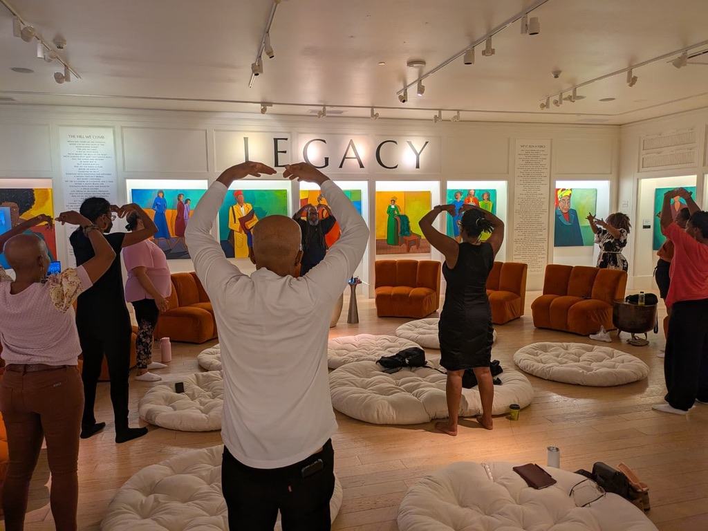 A group practicing a shared hand gesture beneath the Legacy sign