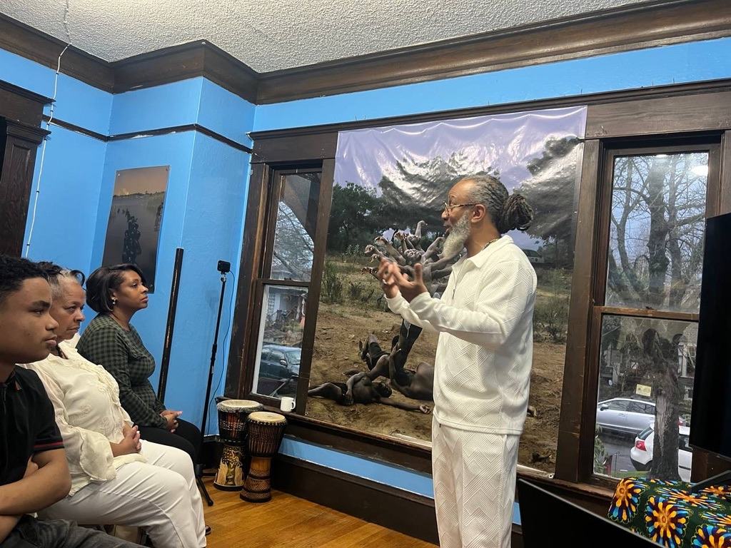 Heru TchaasAmen teaching in a room with djembe drums